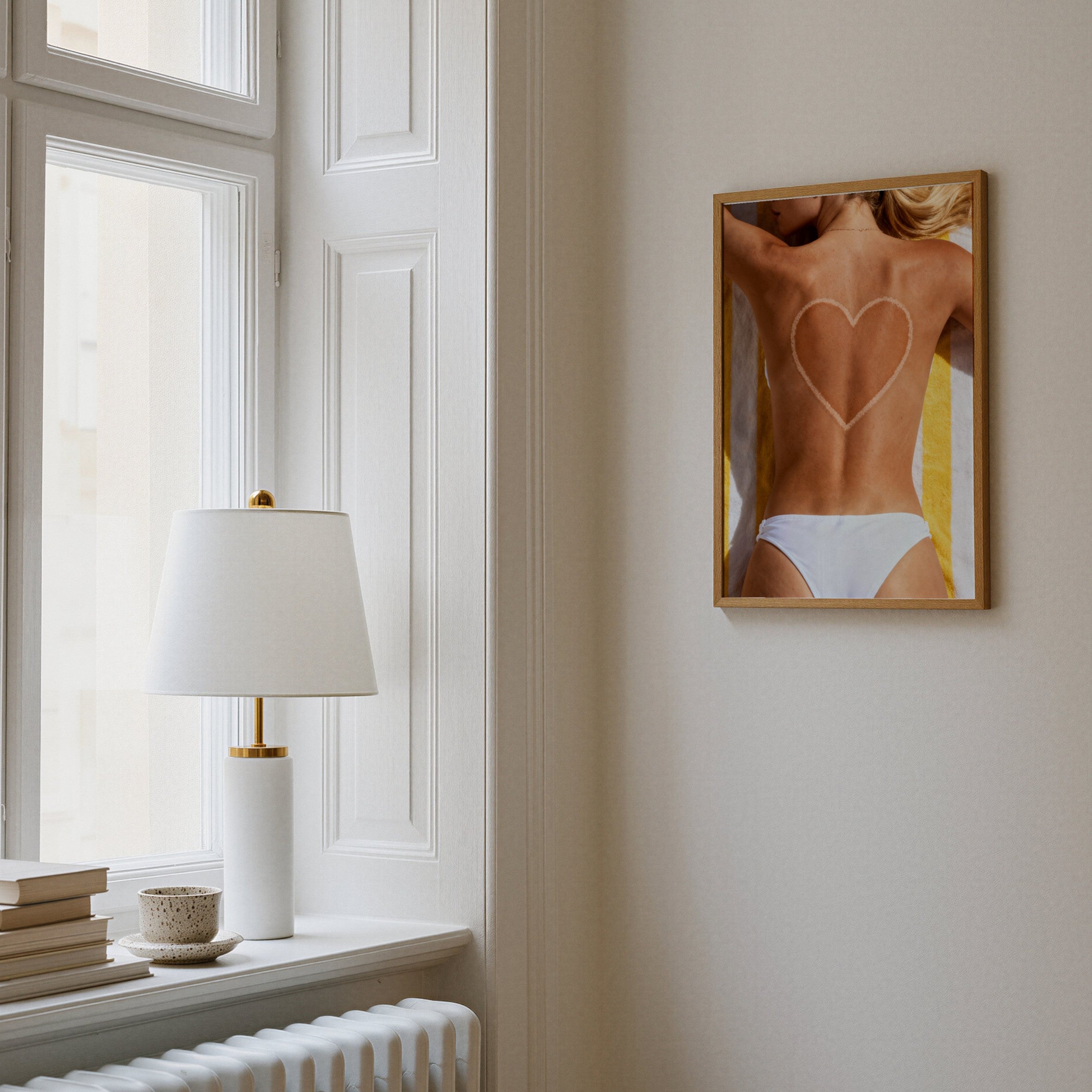 Framed artwork of a person with a heart design on a wall next to a window with a lamp.