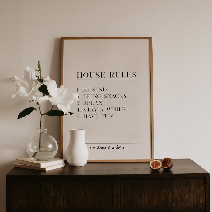 Framed 'House Rules' poster on a wooden surface with decorative items.