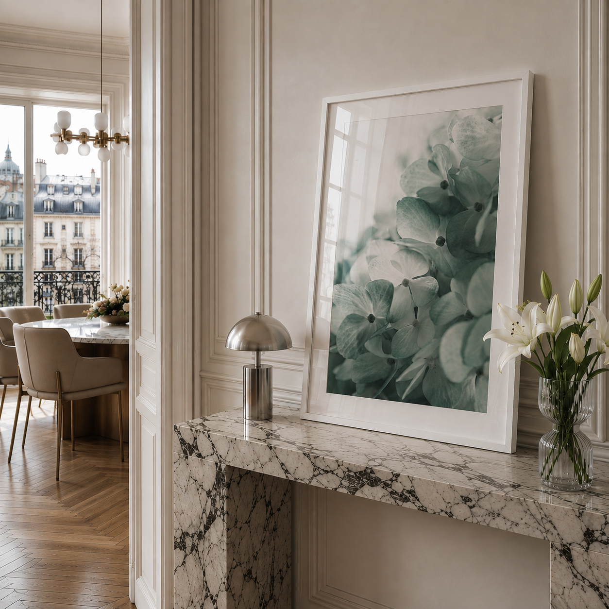 A framed botanical art print featuring soft green hydrangea-like flowers in a white frame, displayed on a marble console table in a stylishly decorated room.