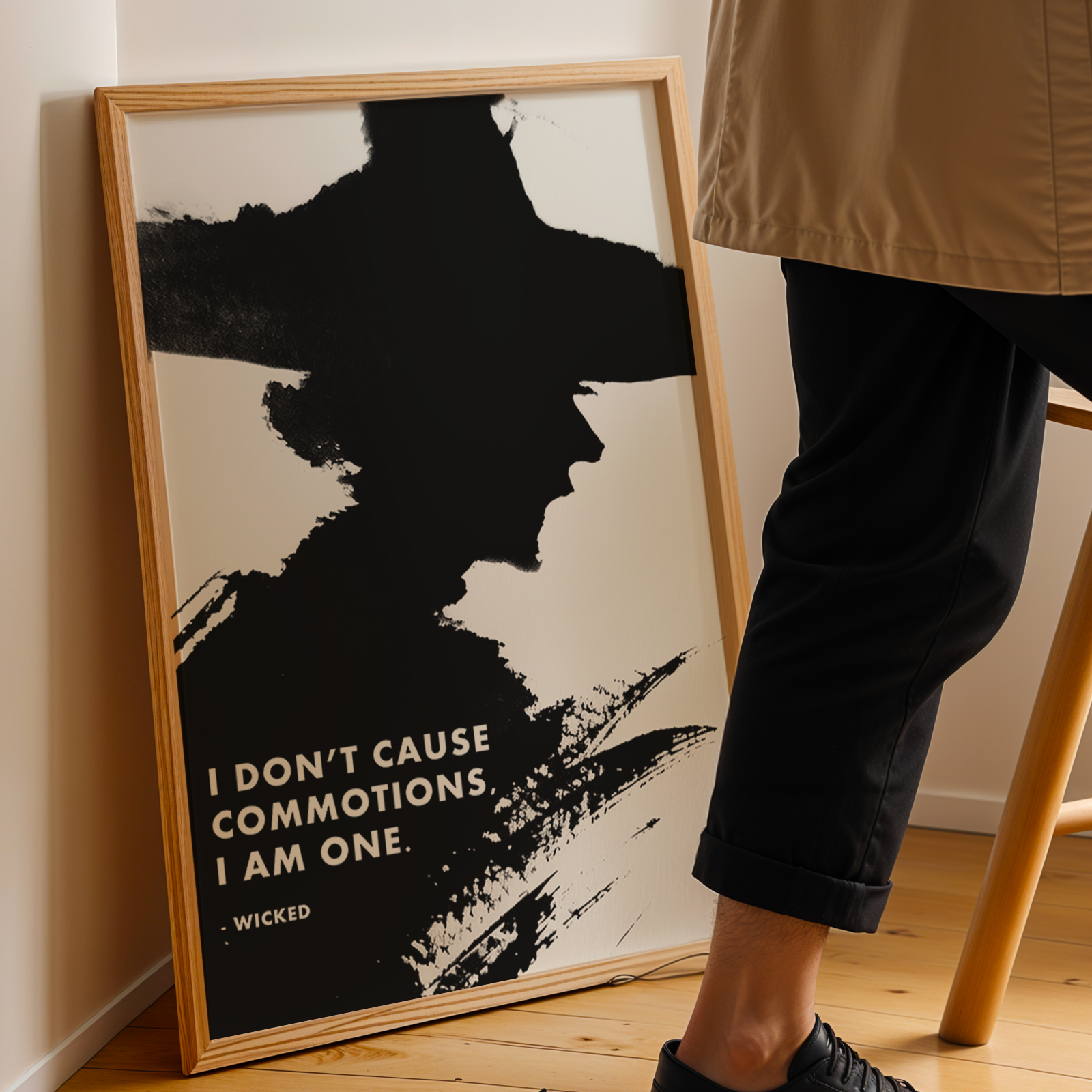 Framed Wicked Movie artwork with a quote on a wall next to a person wearing a beige jacket and black pants.