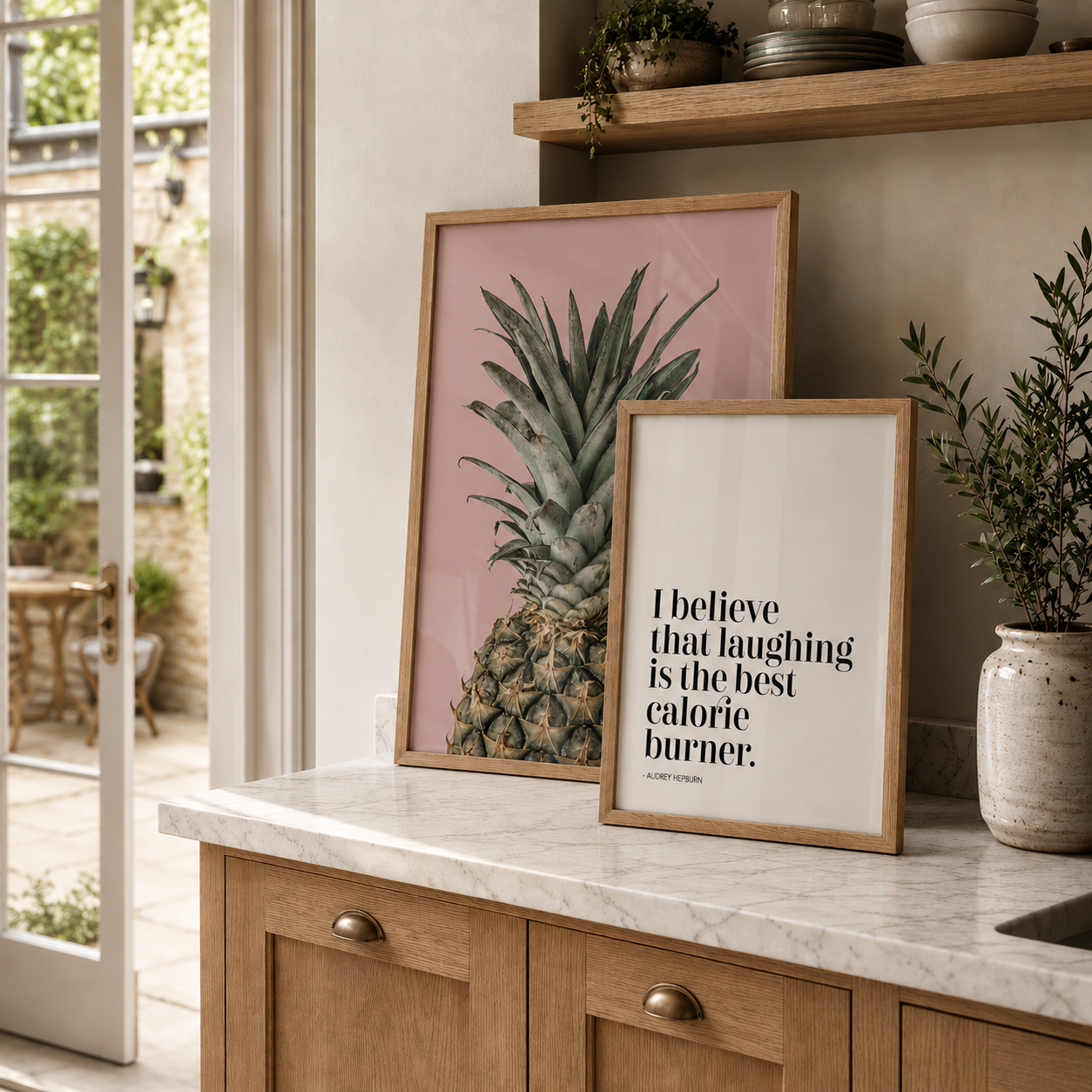Framed pineapple poster and motivational quote on a kitchen counter with plants and a window in the background.