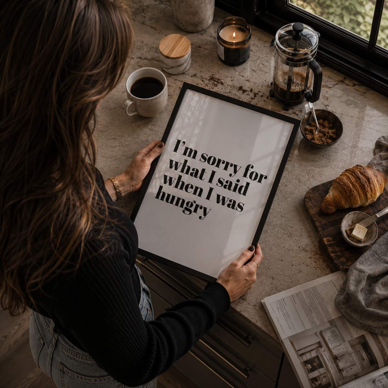 Person holding a framed quote on a kitchen counter with coffee and pastries.