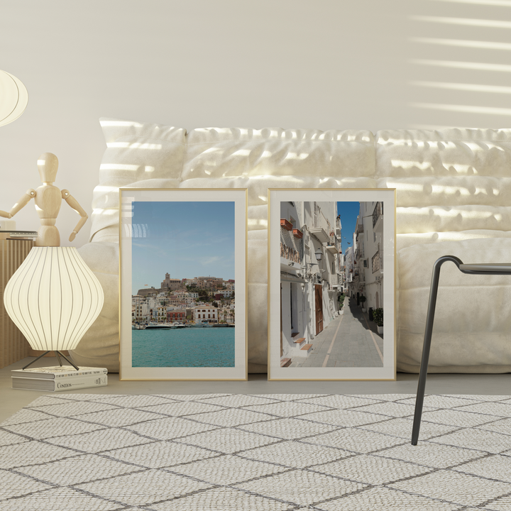 Two framed Ibiza artworks on a wall with decorative lights and a lamp.