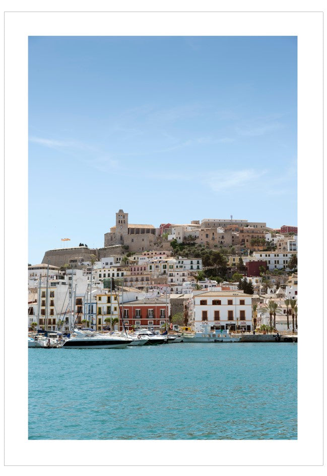 Cityscape with buildings and a castle overlooking a harbor with boats.