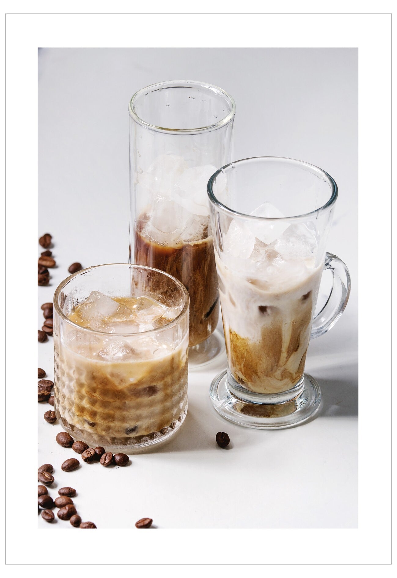 Three glasses of iced coffee with coffee beans on a white surface