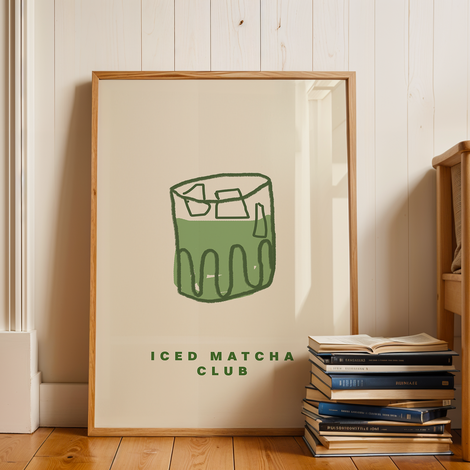 Framed print of 'ICED MATCHA CLUB' with a stack of books on a wooden floor.