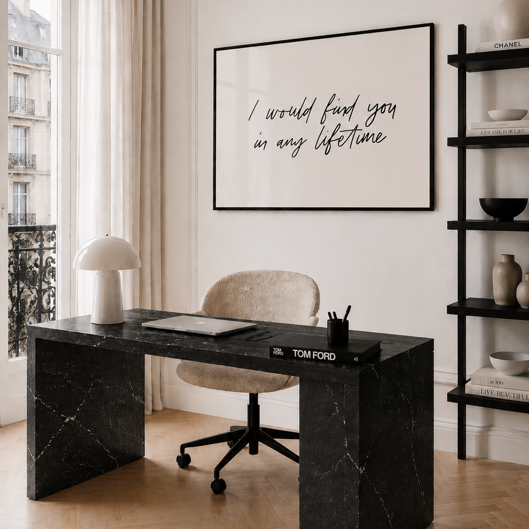 Modern home office with black marble desk, beige chair, and framed quote on wall.