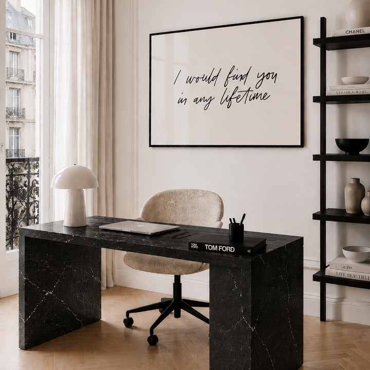 Modern home office with black marble desk, beige chair, and framed quote on wall.