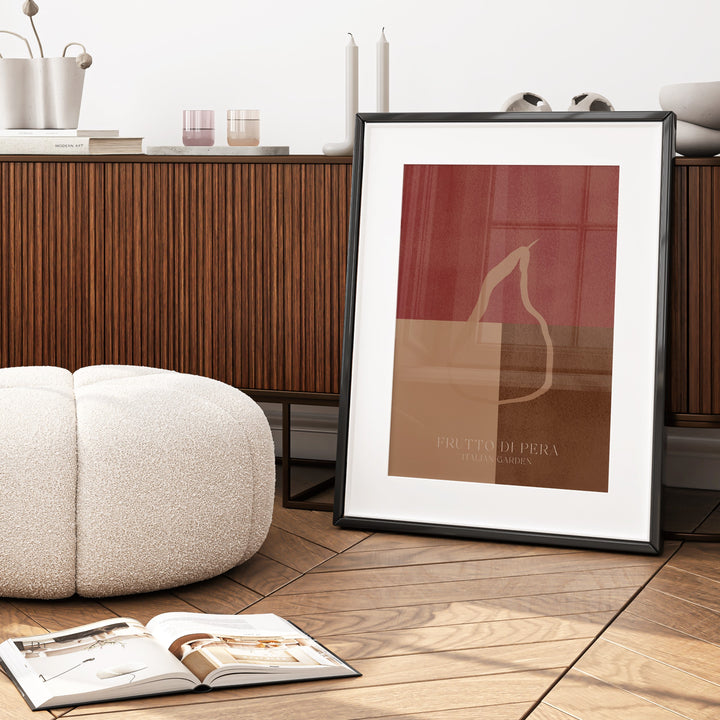 Framed abstract art print on a wooden floor with a white ottoman and open book.
