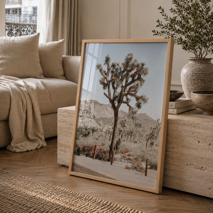A framed art print depicting a desert landscape with a Joshua tree and mountains, leaning against a stone side table in a cozy living room setting.
