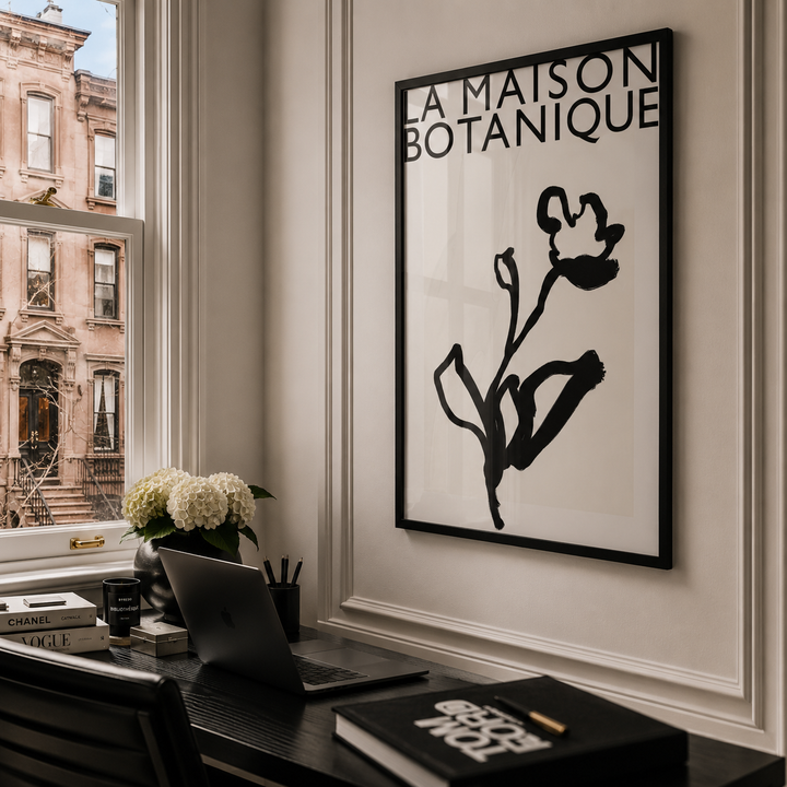 Modern office interior with a framed artwork of a black flower on a white background, books, and a laptop.