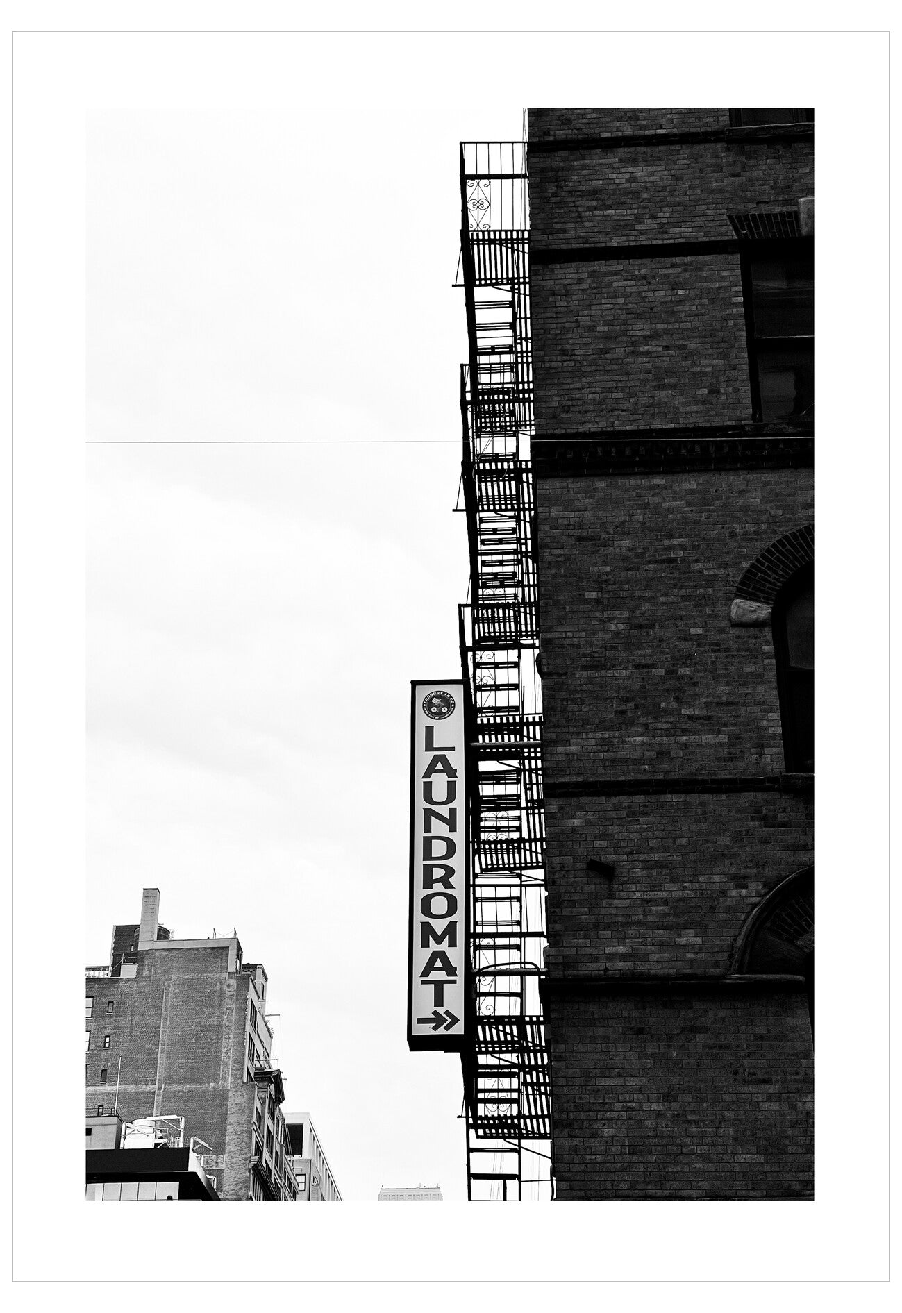 Black and white photo of a building with a fire escape and 'Laundromat' sign.