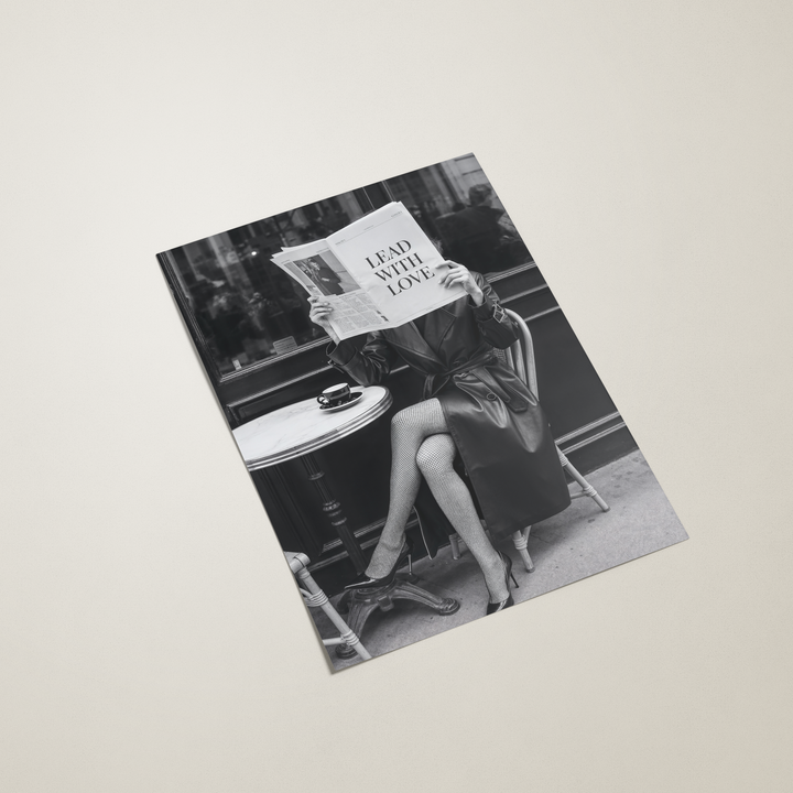 poster with a black and white photo of a woman sitting at a table with a newspaper, on a light gray background.