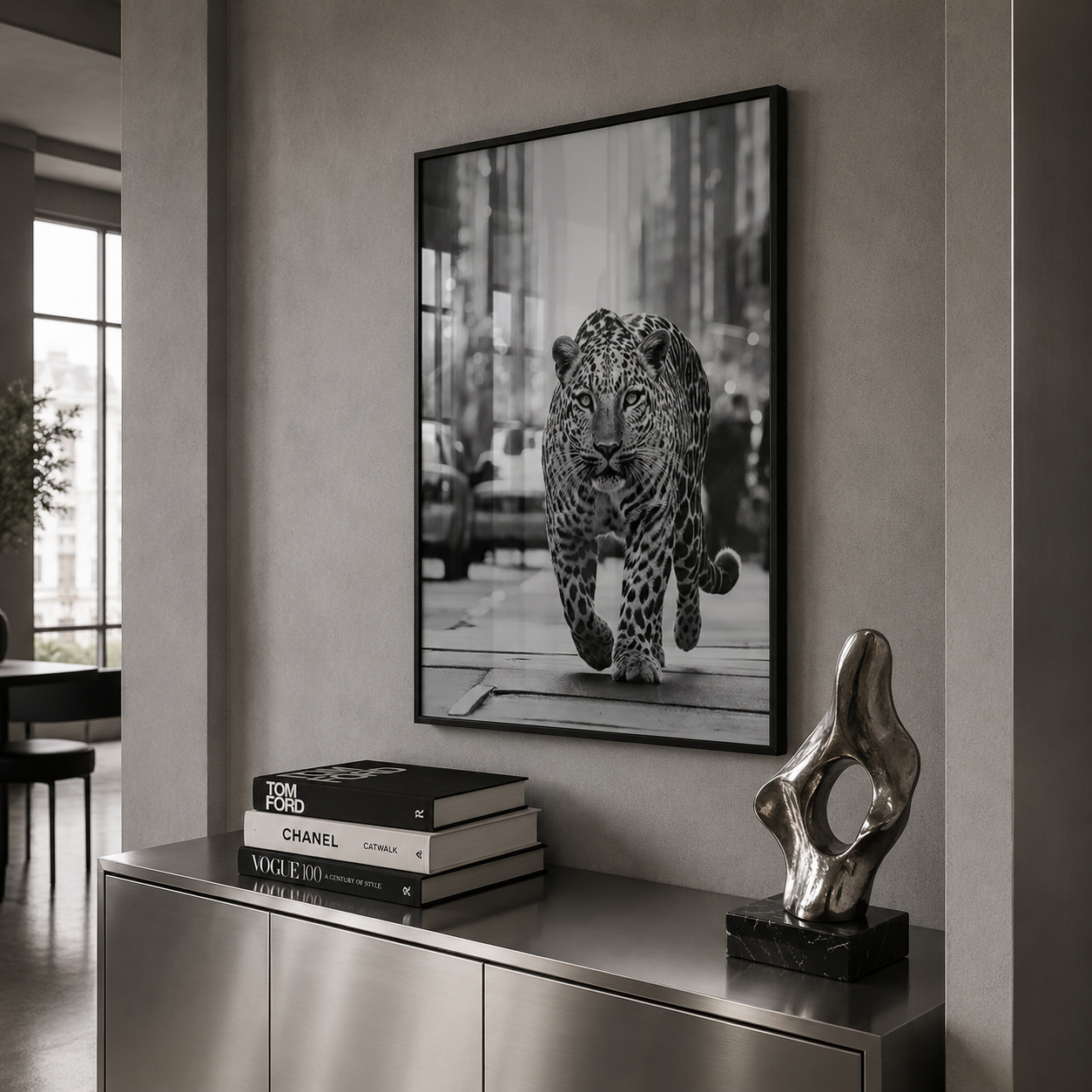 Framed artwork of a leopard on a wall above a metallic console table with books and a sculpture.