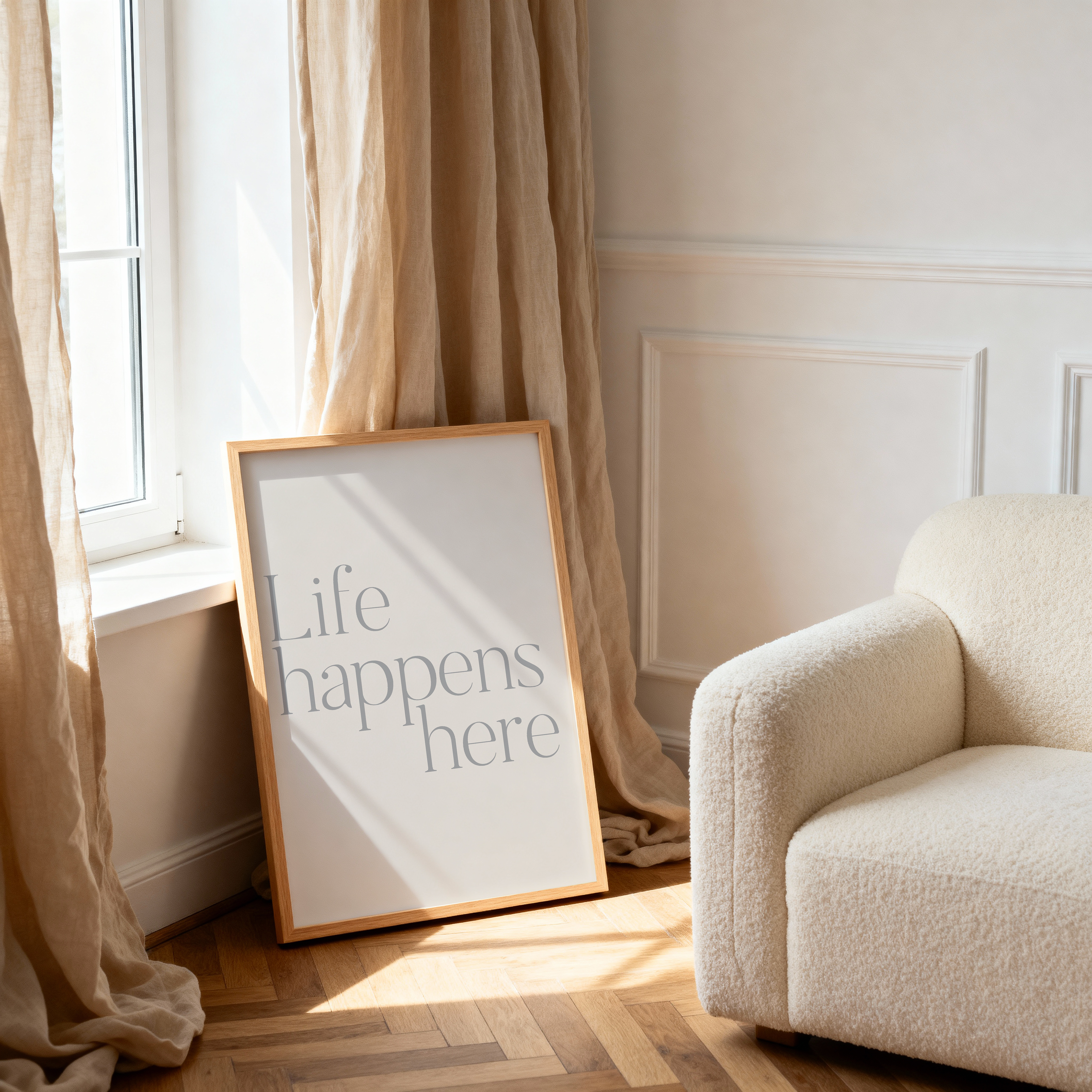 Framed poster with 'Life happens here' text on a wooden floor next to a beige armchair.