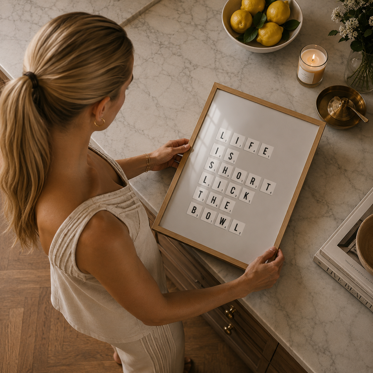 Woman holding a framed quote on a kitchen counter with lemons and a candle in the background.