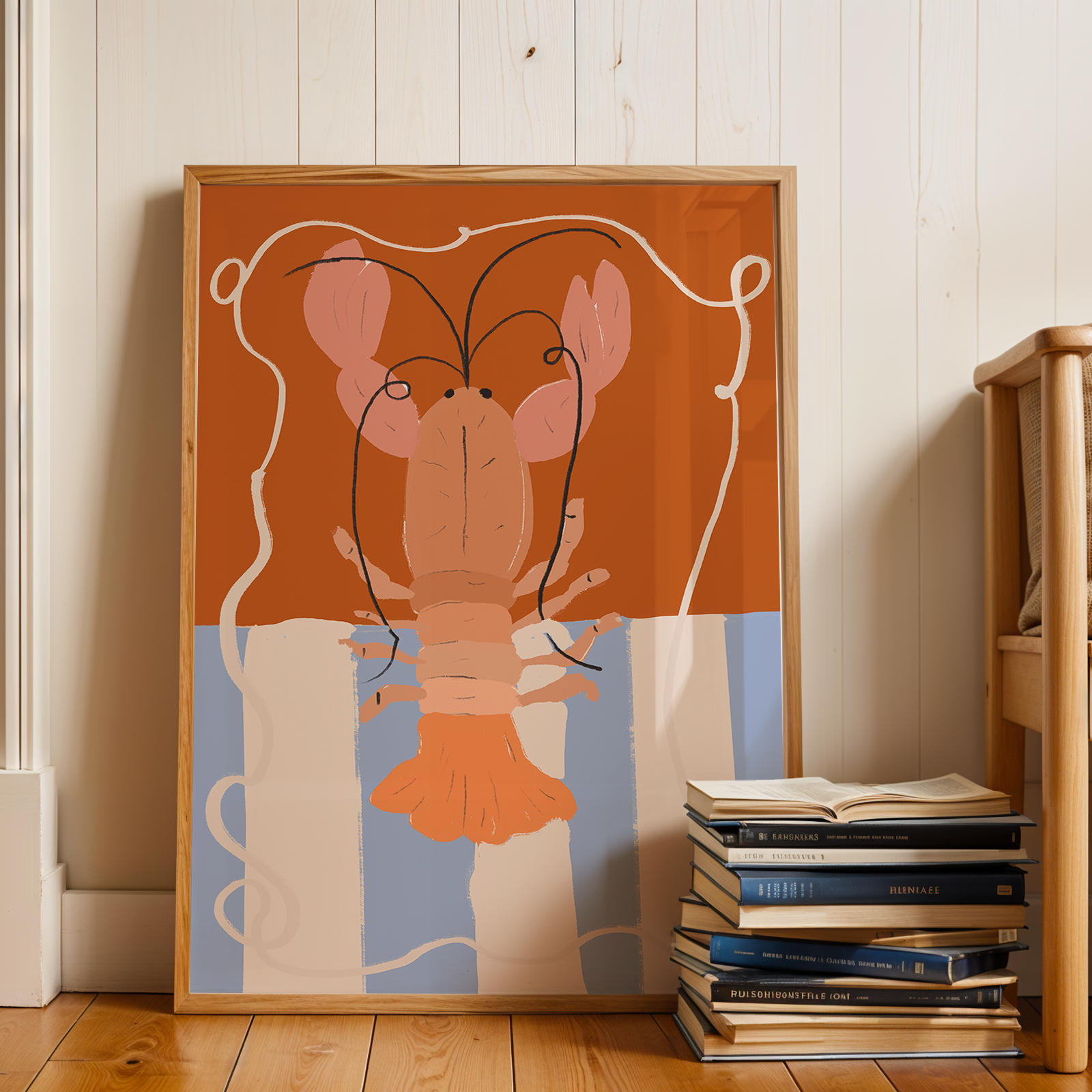 Framed artwork of a stylized lobster on a wall next to a stack of books and a wooden chair.