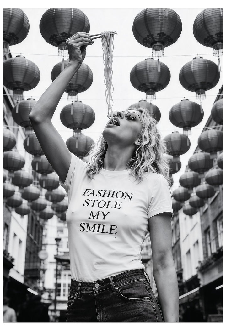 Woman eating noodles wearing a t-shirt with 'Fashion stole my smile' text in Chinatown with hanging lanterns.