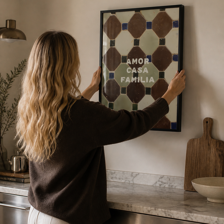 Woman hanging a framed artwork on a wall in a kitchen.