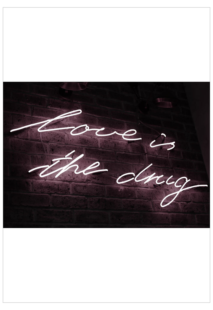 Neon sign with 'Love is the drug' on a brick wall