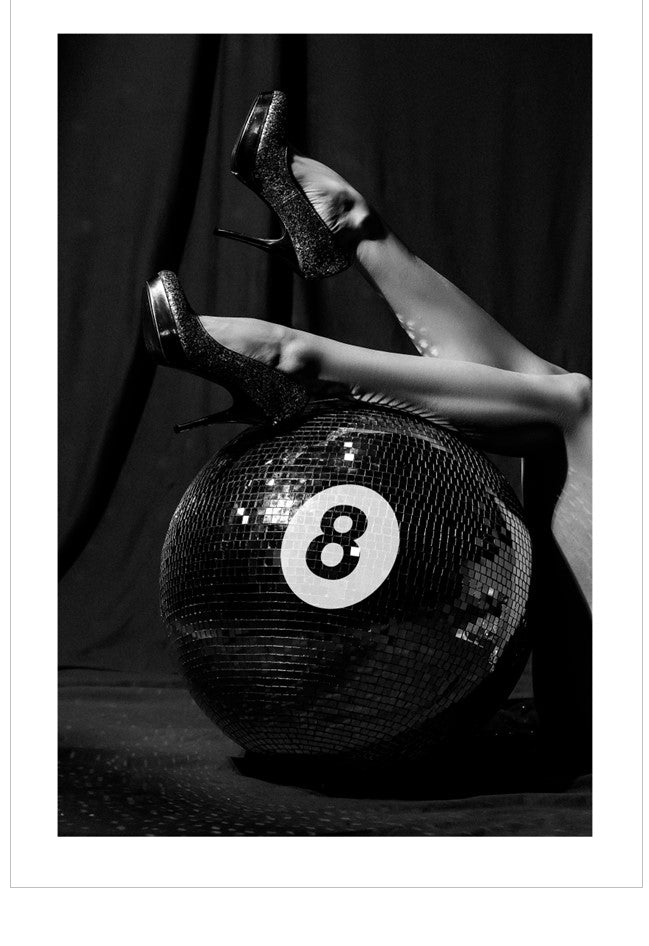 Person wearing high heels stepping on a disco ball with number 8, black and white photo