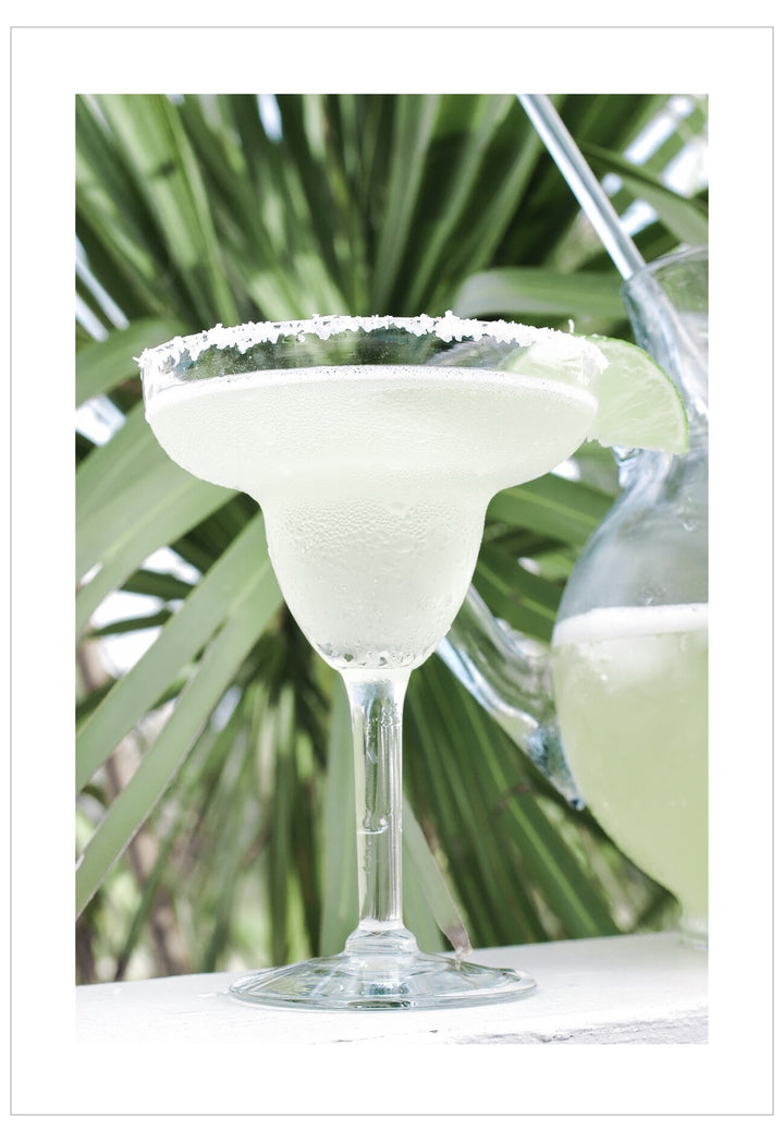 Glass of margarita with salted rim against a palm leaf background