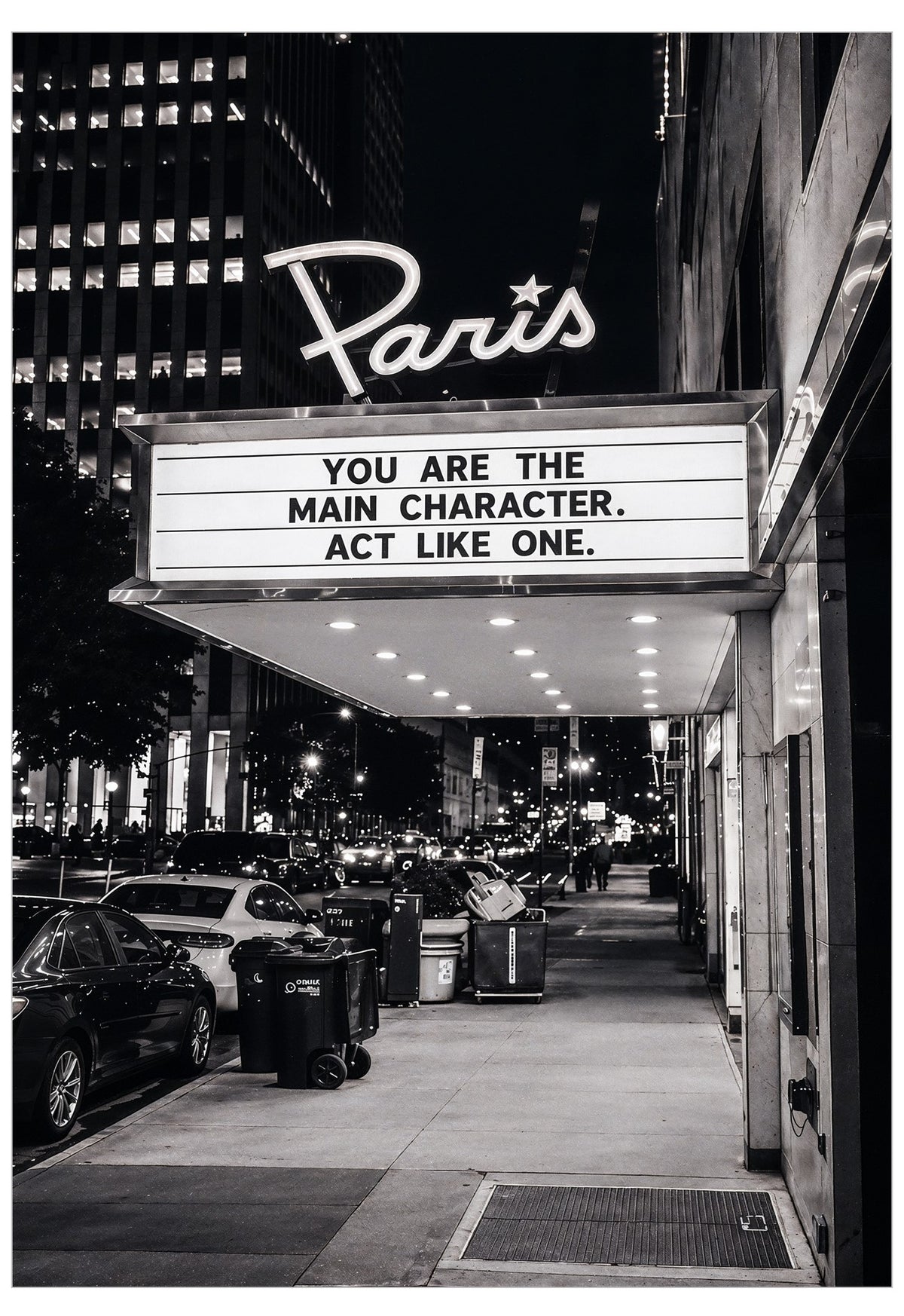 Black and white photograph of a Paris-themed movie theater marquee at night, with the sign reading 'YOU ARE THE MAIN CHARACTER. ACT LIKE ONE.