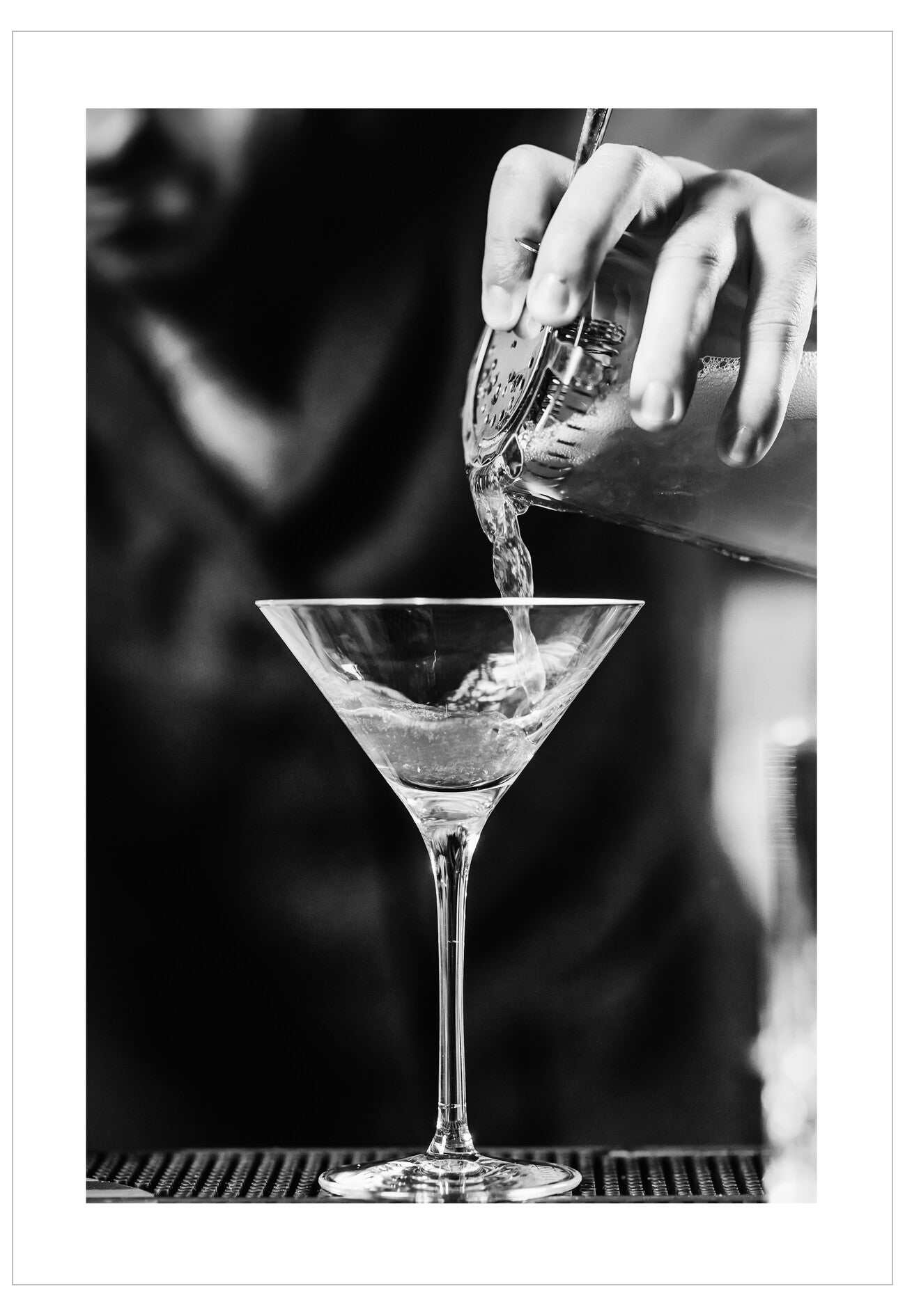 Person pouring a drink into a martini glass with a blurred background