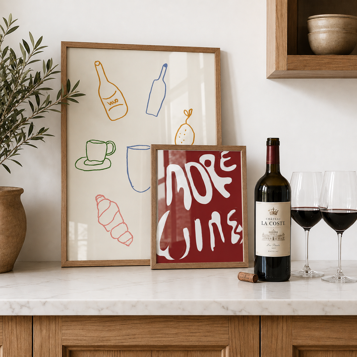 Framed artwork on a kitchen counter with a bottle of wine and glasses.