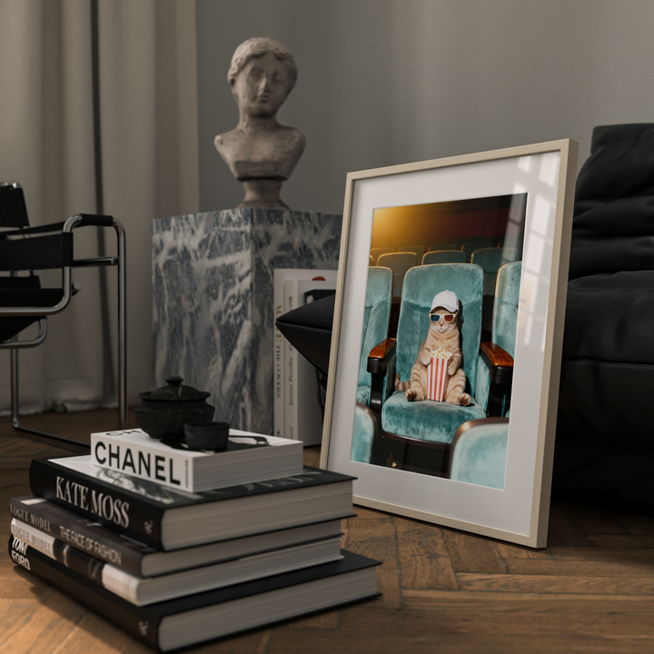 Framed picture of a cat wearing sunglasses on a table with books and a bust in the background.