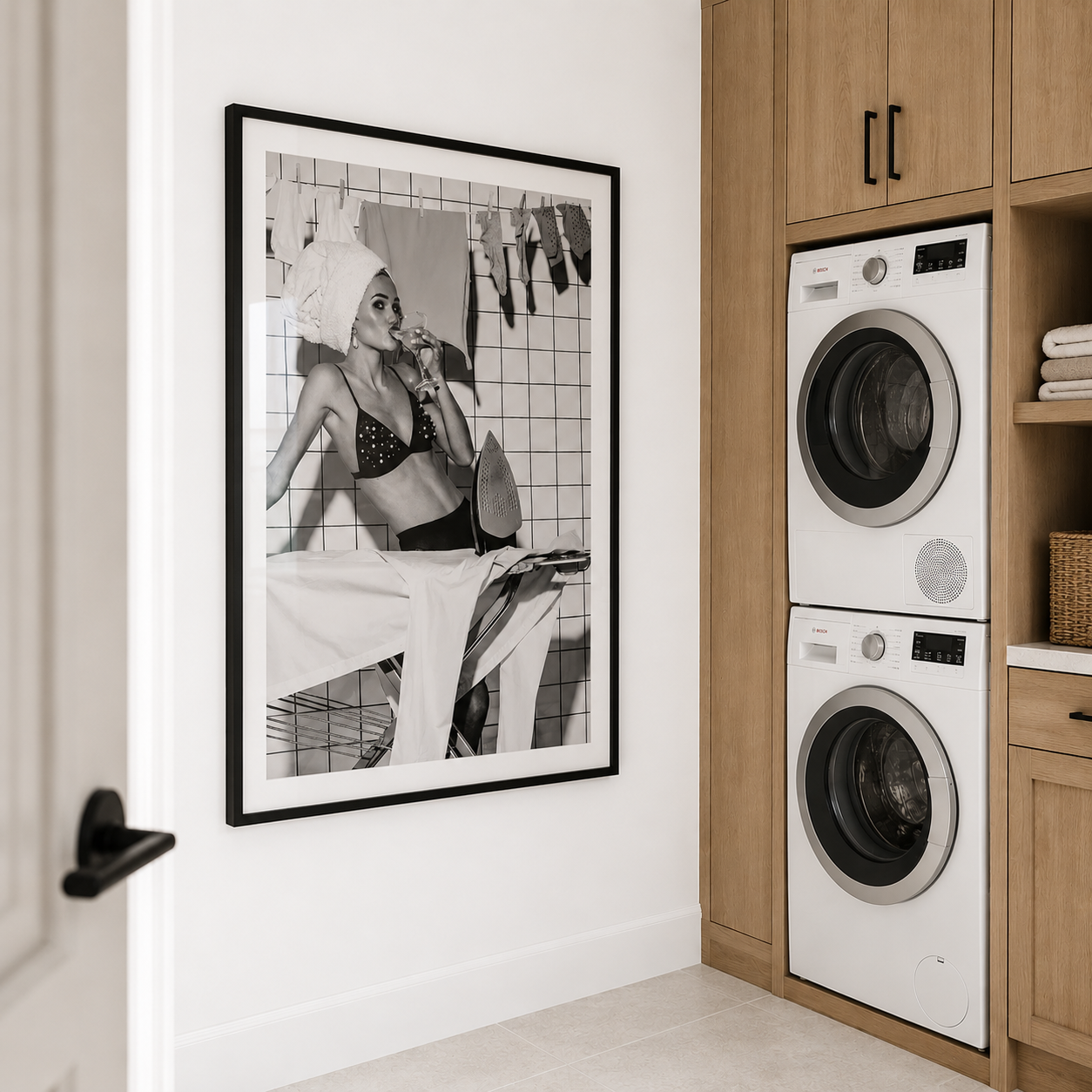 Laundry room with stacked washer and dryer, framed black and white art on wall, wooden cabinets.