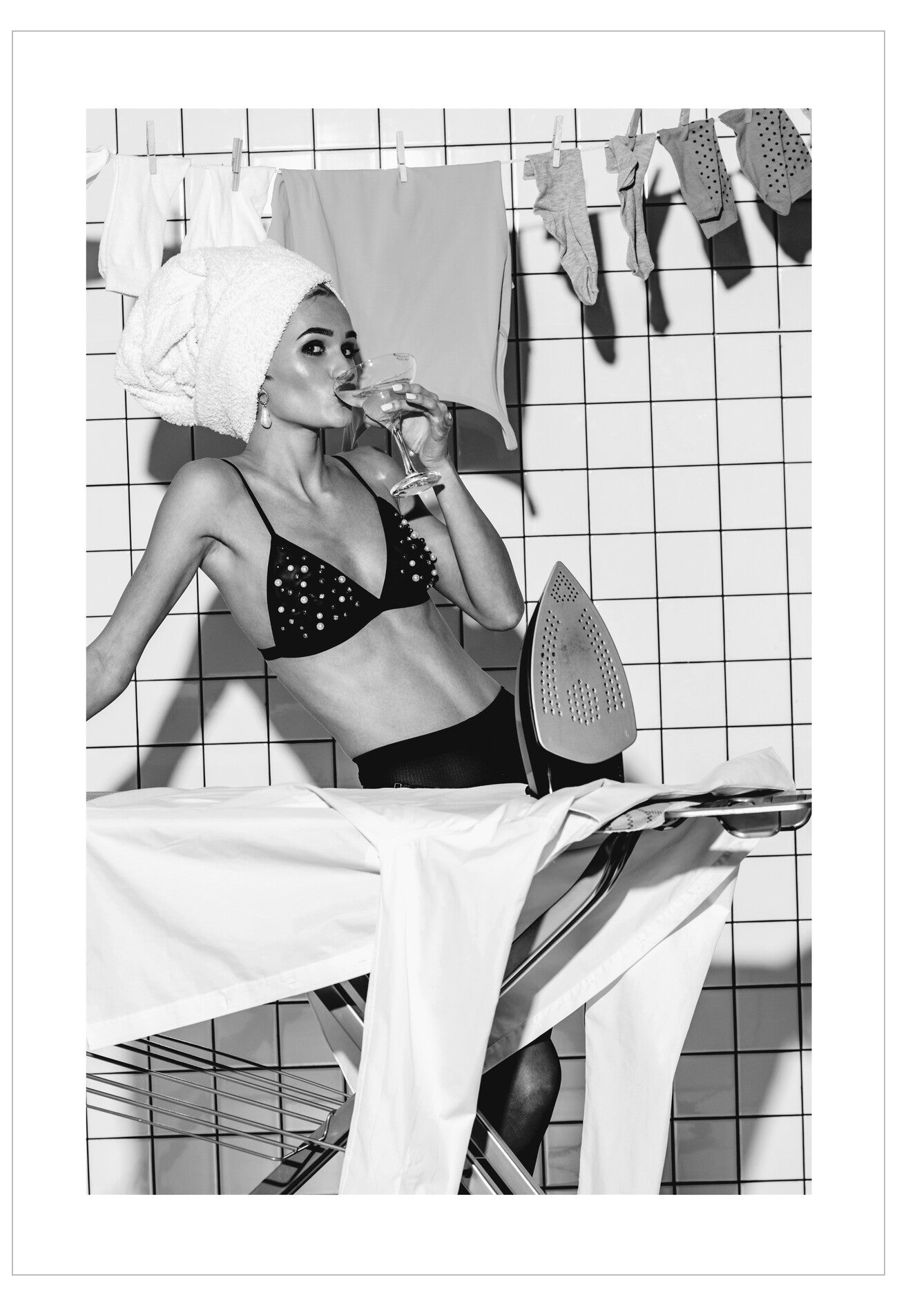 Woman in a black bra and panties sitting on a chair with a glass of wine, surrounded by laundry.