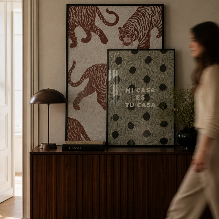 Woman walking past a wooden cabinet with decorative items including framed pictures and a lamp.