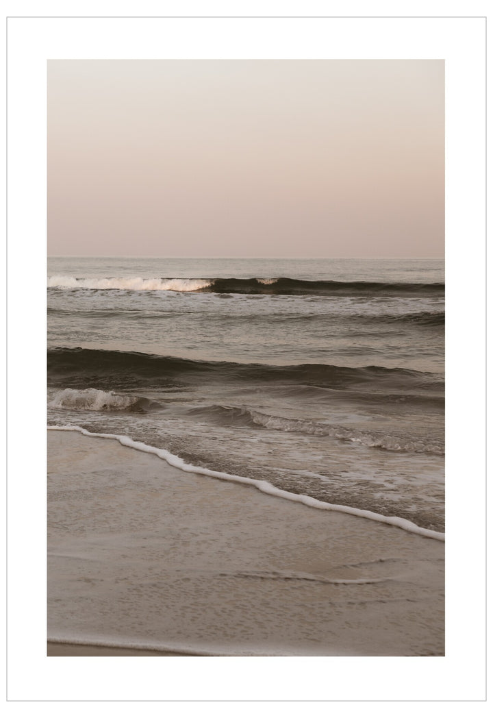 Waves crashing onto a beach with a pastel sky