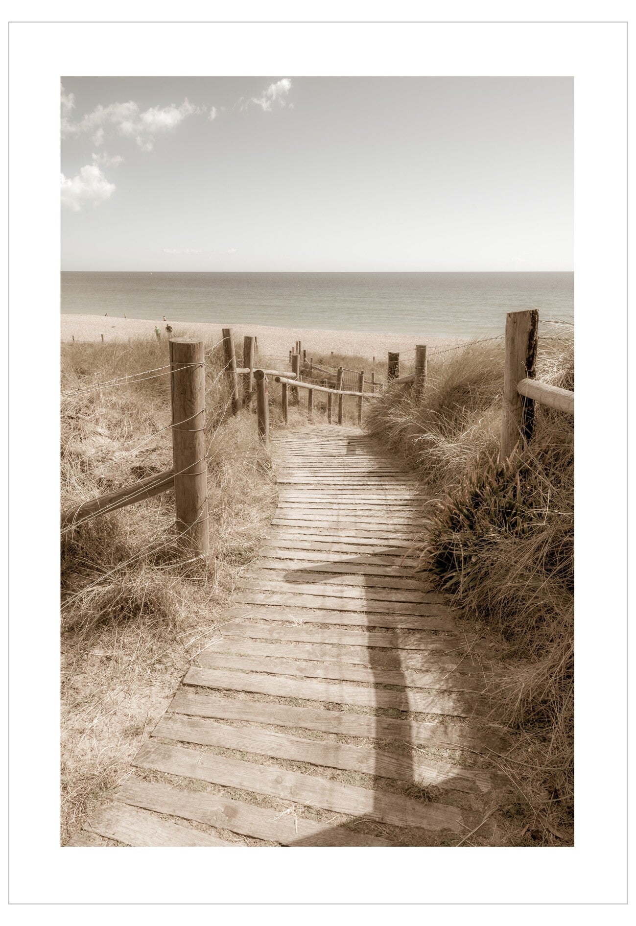 Wooden pathway leading to a beach with grass and wooden posts on a cloudy day.