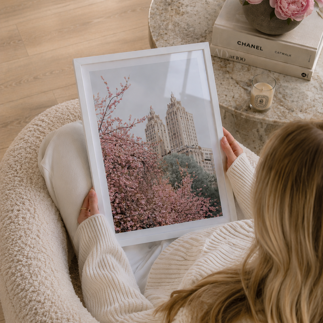 Person holding a framed picture of cherry blossoms and a cityscape, sitting on a couch.