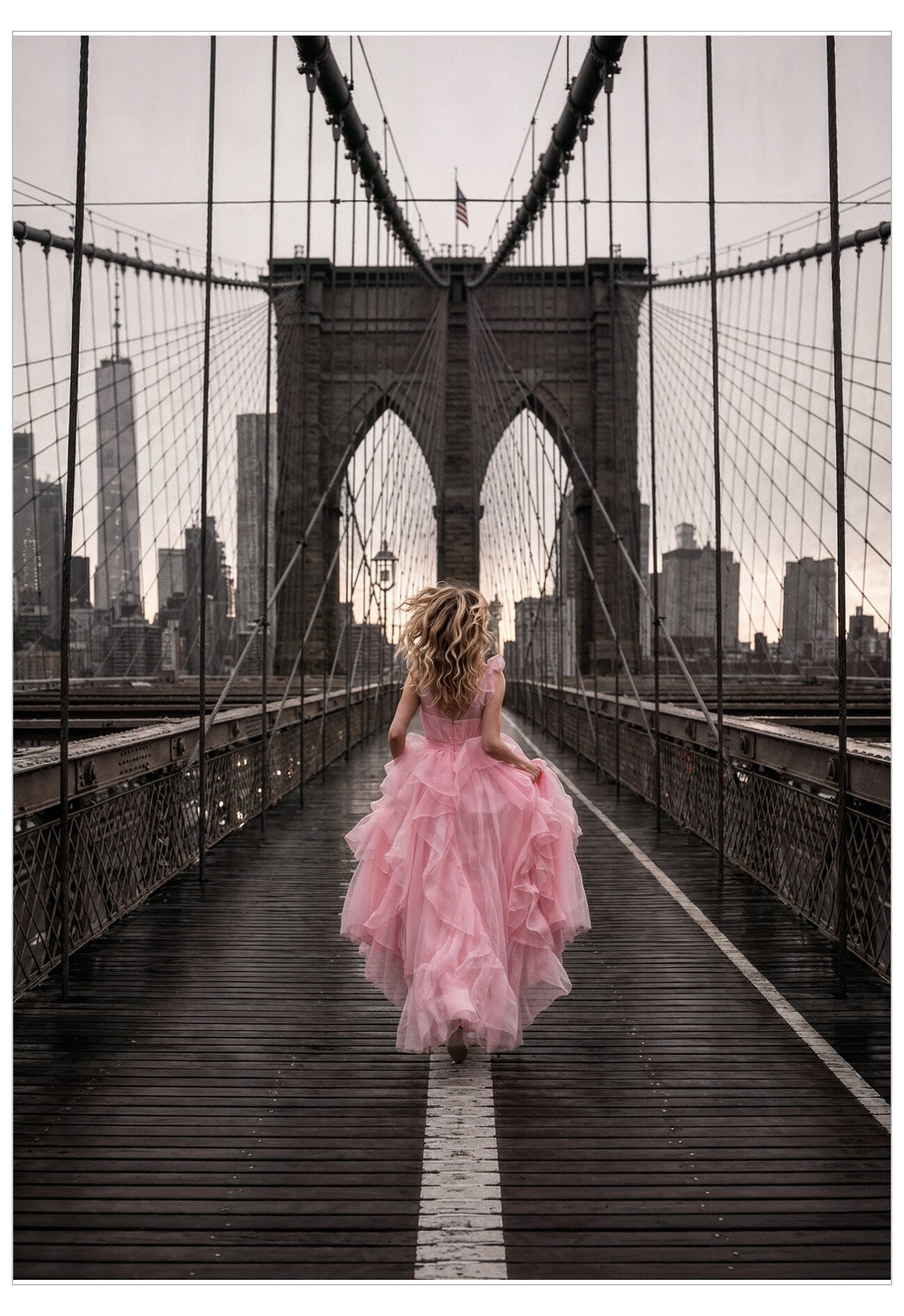 Woman in a pink dress walking on the Brooklyn Bridge with a city skyline in the background