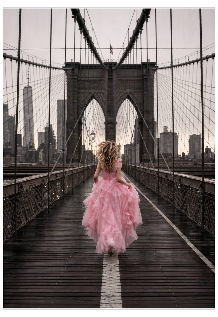 Woman in a pink dress walking on the Brooklyn Bridge with a city skyline in the background