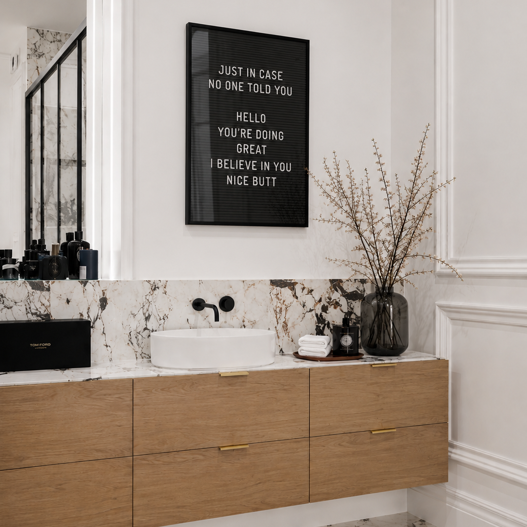 Bathroom with wooden vanity, marble countertop, and framed quote on the wall.
