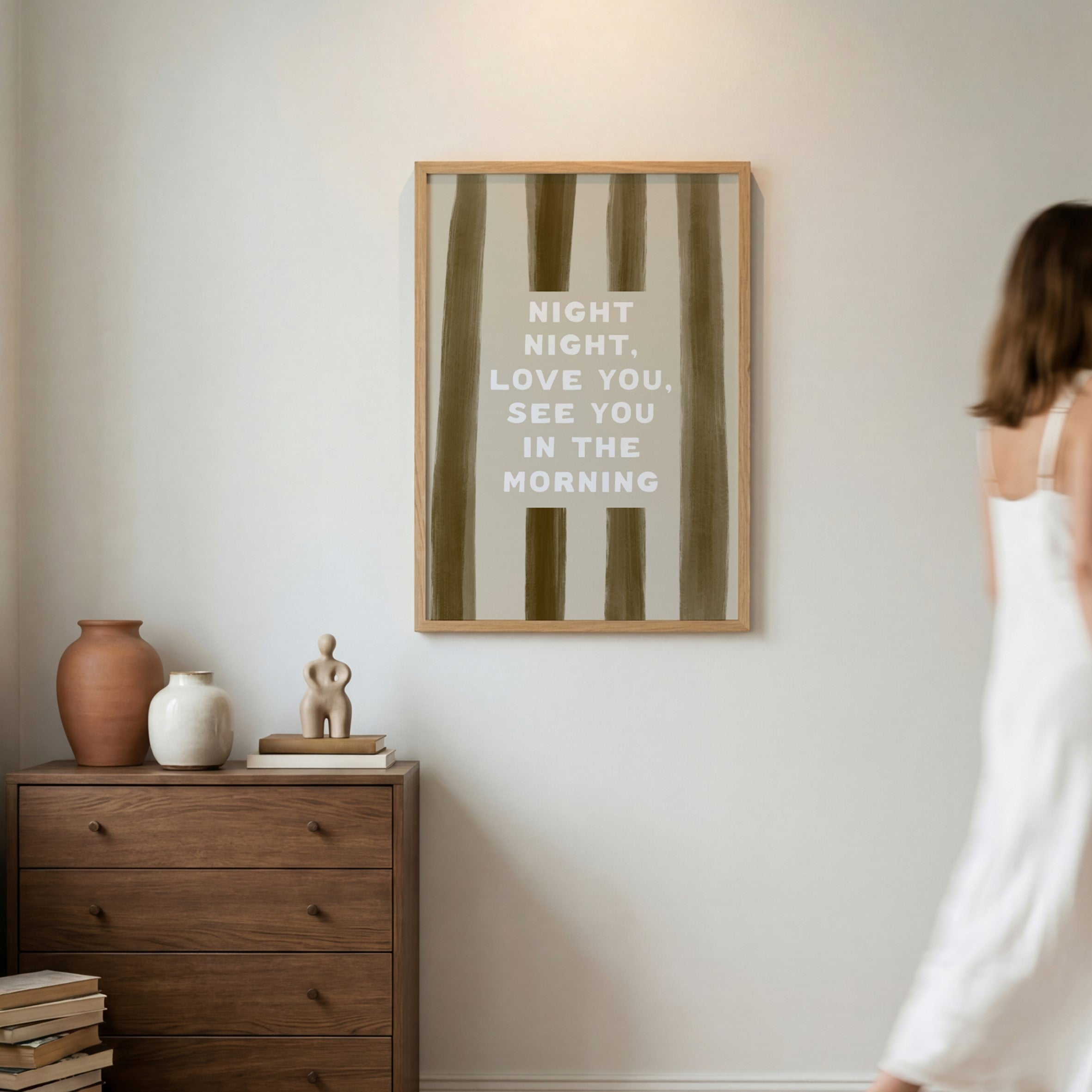 Framed artwork with text on a wall above a wooden dresser with decorative items.