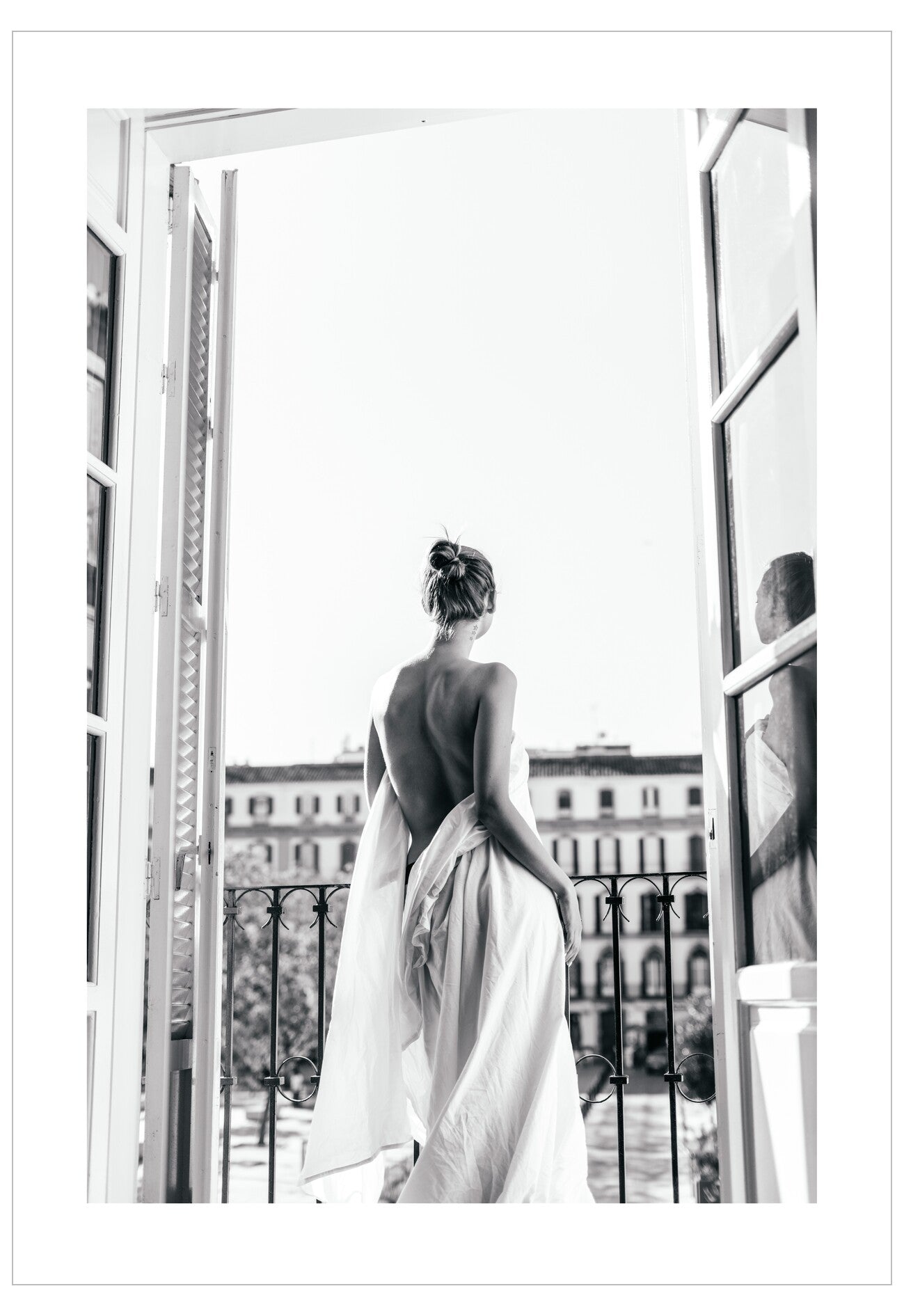 Woman in a flowing dress standing by an open window with a cityscape view.