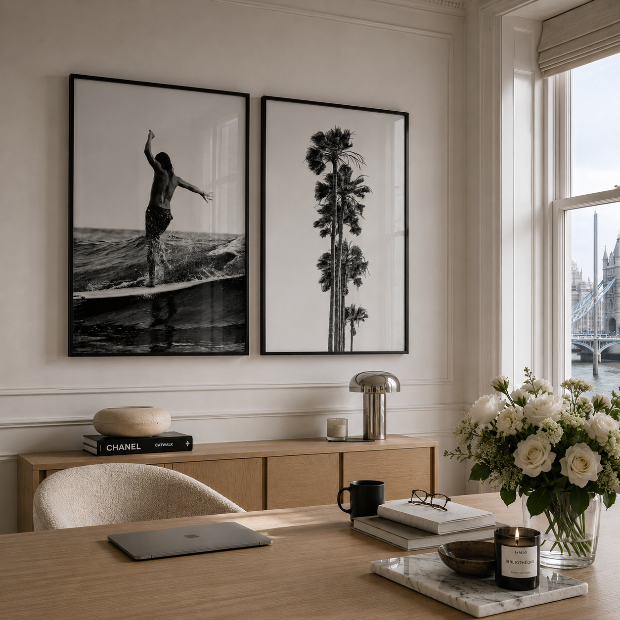 Two framed black-and-white wall art prints hang above a wooden console in a bright, modern room. The left print shows a surfer on a wave, and the right print shows tall palm trees.