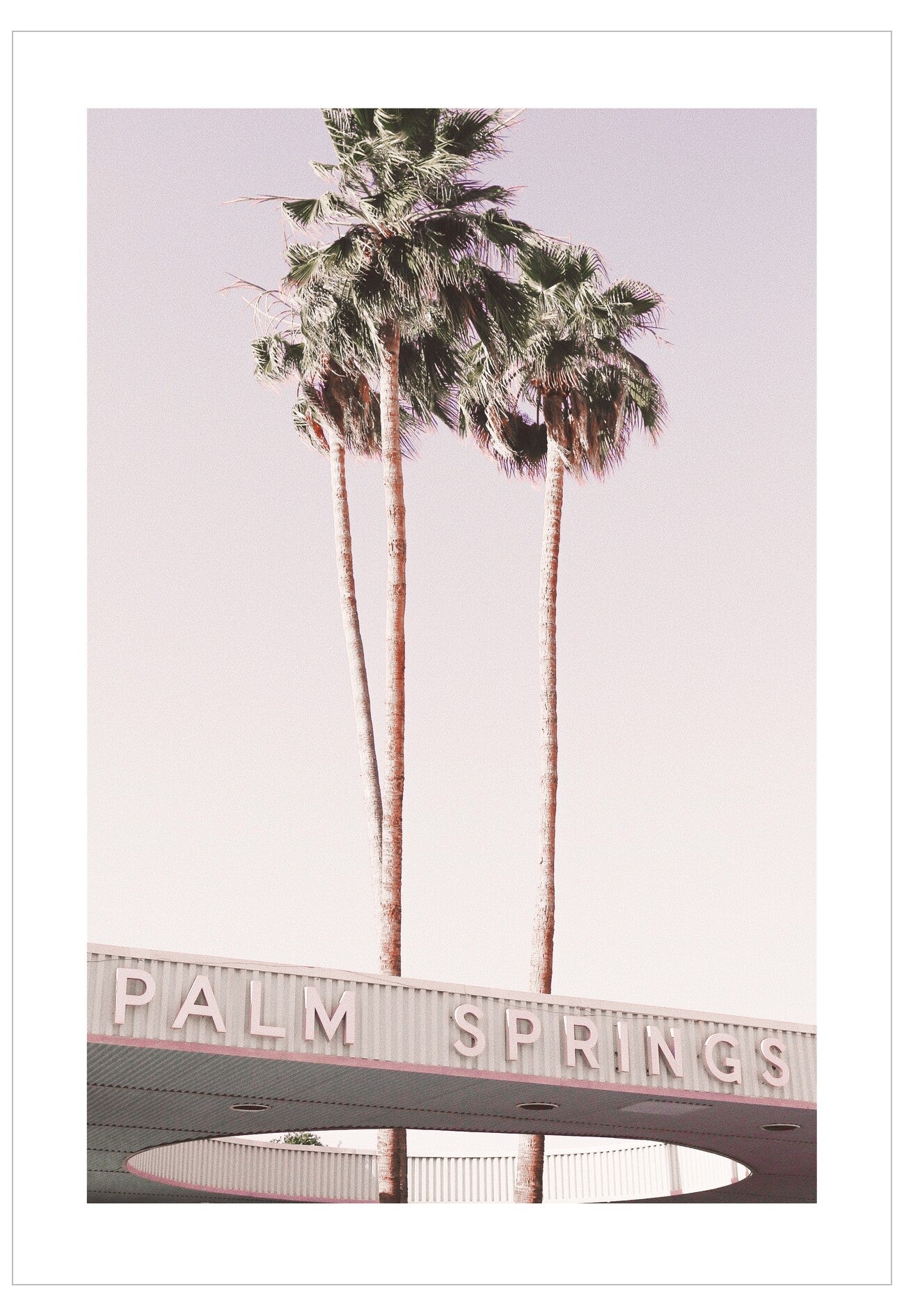 Palm Springs sign with palm trees against a light pink sky