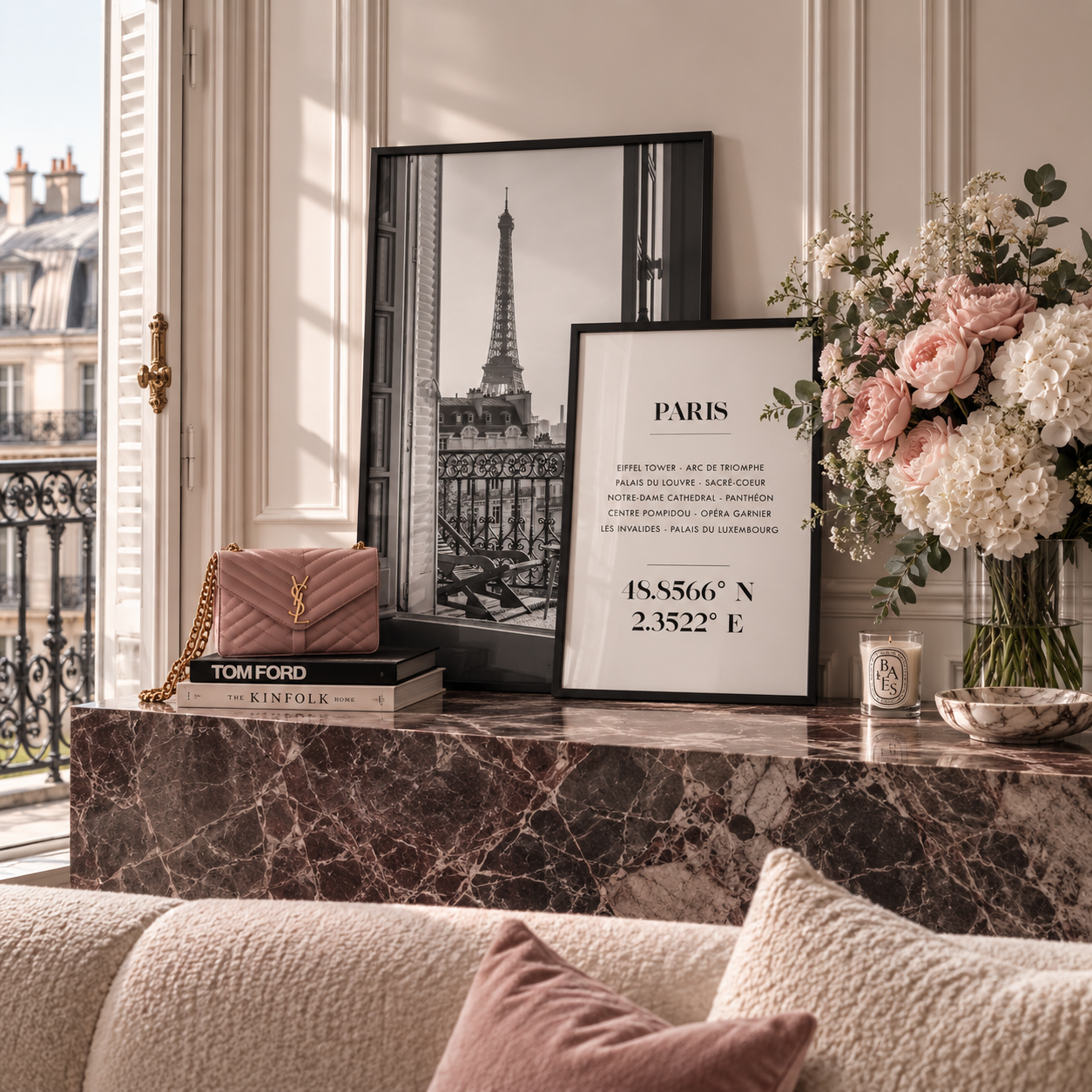 A styled interior scene with framed wall art leaning on a marble console table. The most prominent sellable subject appears to be the Paris-themed framed print/poster in the center-right, showing a black-and-white Eiffel Tower image and Paris coordinates, with additional decor including flowers, a pink quilted handbag, books, and a candle in a nearby room.