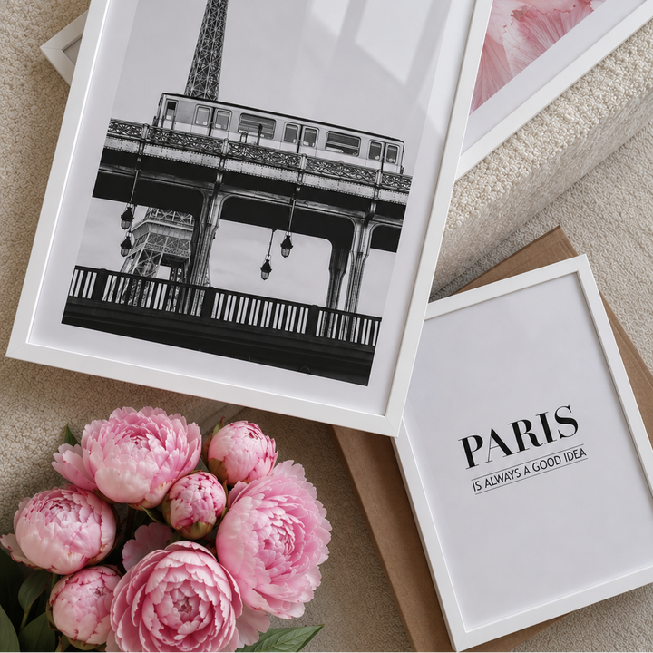 Framed prints of a train under a bridge and 'Paris is always a good idea' with pink flowers on a textured surface.