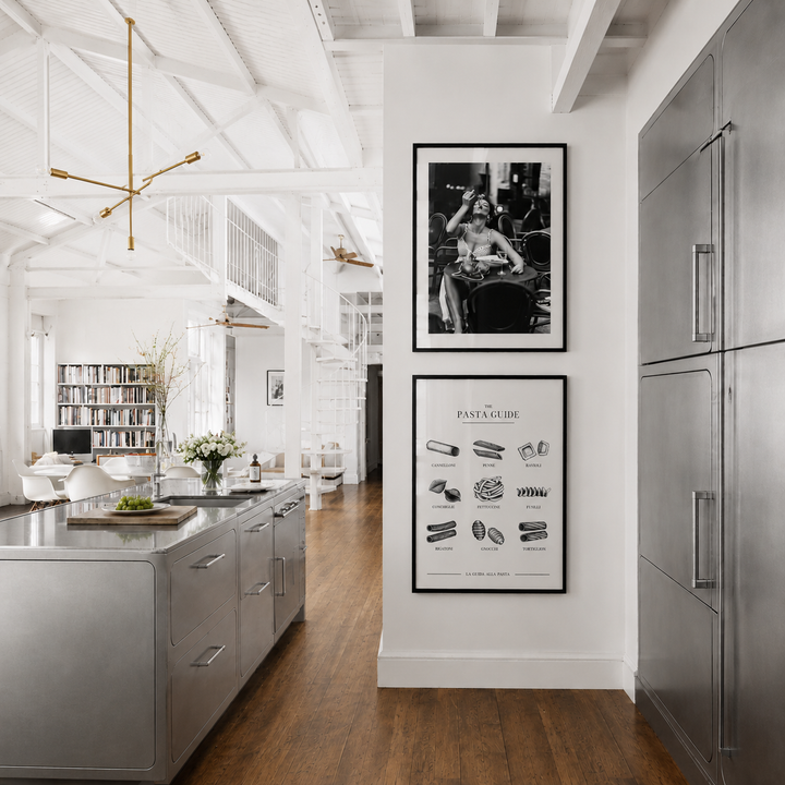 Modern kitchen with stainless steel appliances, wooden floor, and framed artwork on the wall.