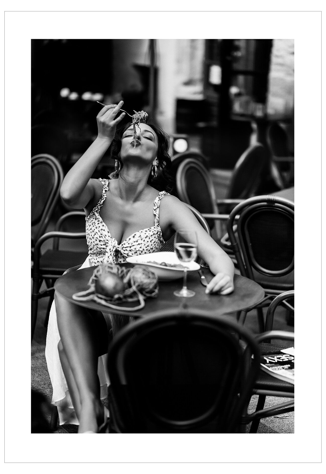 Woman sitting at an outdoor table eating a flower, black and white photo