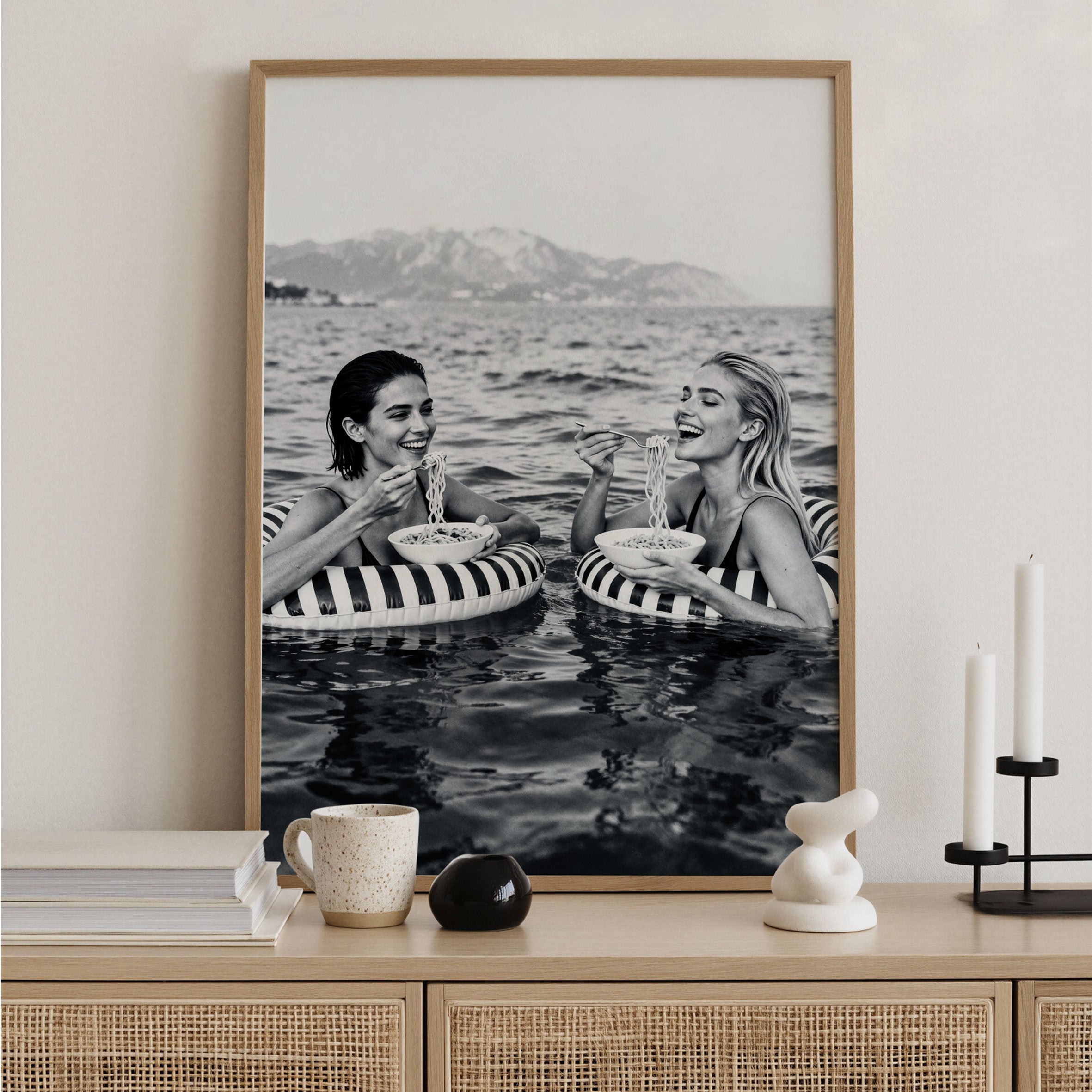 Framed black and white photograph of two women in striped swimsuits enjoying food and drinks in the water.