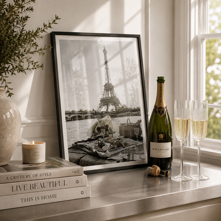 Bottle of Bollinger champagne with two glasses on a table next to a framed picture of the Eiffel Tower.