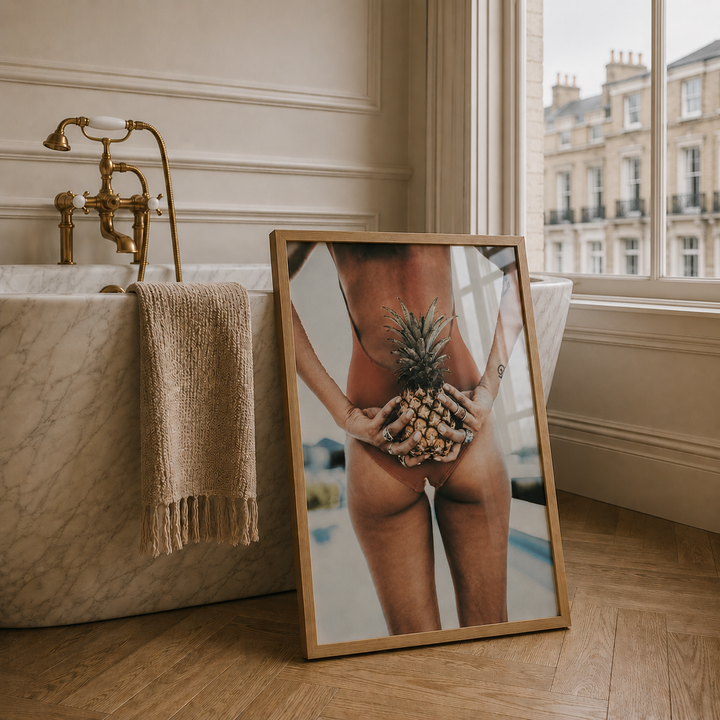 Framed artwork of a person holding a pineapple in a bathroom setting